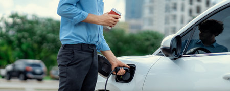 Closeup progressive man holding EV charger plug from public charging station for electric vehicle with background of residential building as concept eco-friendly sustainability energy car concept.の写真素材
