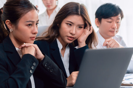 Focused businesspeople using laptop working on data analysis with serious facial expression in corporate environment at harmony office. Struggle in financial strategy planning at meeting desk.の写真素材