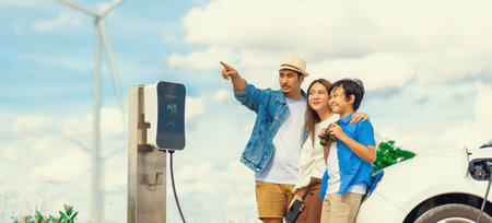 Concept of progressive happy family enjoying their time at wind farm with electric vehicle. Electric...