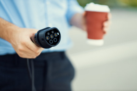 Focus on EV charging plug device from charging station for electric vehicle with blurred man holding plug and pointing at the camera background for alternative renewable energy.の写真素材