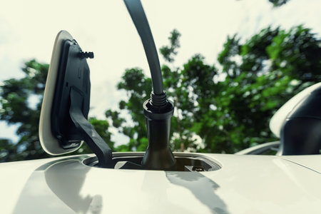 Closeup EV charger plugged into electric vehicle socket at charging station image from below view as progressive concept of eco-friendly car powered by sustainable and renewable energy.の写真素材