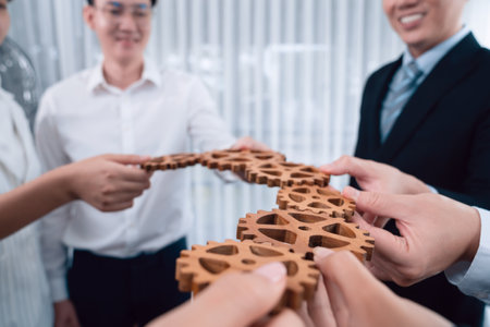 Closeup hand holding wooden gear by businesspeople wearing suit for harmony synergy in office workplace concept. Group of people hand making chain of gears into collective form for unity symbol.の写真素材