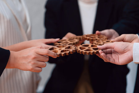 Closeup hand holding wooden gear by businesspeople wearing suit for harmony synergy in office workplace concept. Group of people hand making chain of gears into collective form for unity symbol.の写真素材