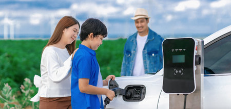 Concept of progressive happy family enjoying their time at wind farm with electric vehicle. Electric...