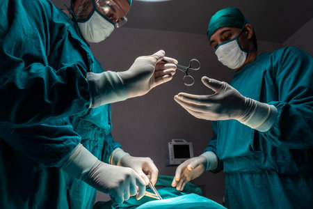 Surgical team performing surgery to patient in sterile operating room. In a surgery room lit by a lamp, a professional and confident surgical team provides medical care to an unconscious patient.の写真素材