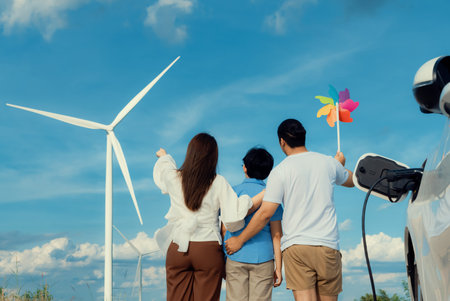 Progressive happy family enjoying their time at wind farm for green energy production concept. Wind turbine generators provide clean renewable energy for eco-friendly purposes.の写真素材