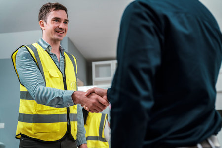 An engineer with a protective vest handshake with an investor in his office. Following a successful...