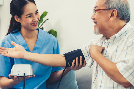 A contented retired man having a blood pressure check by his personal caregiver at his home with a smiley face. Senior care at home, nursing home for pensioners.の写真素材