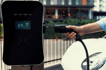 Closeup progressive man holding EV charger plug from public charging station for electric vehicle...