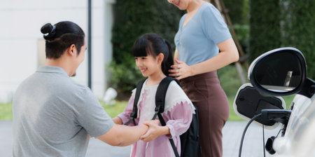 Progressive young parents and daughter with electric vehicle and home charging station. Green and clean energy from electric vehicles for healthy environment. Eco power from renewable source at home.の写真素材