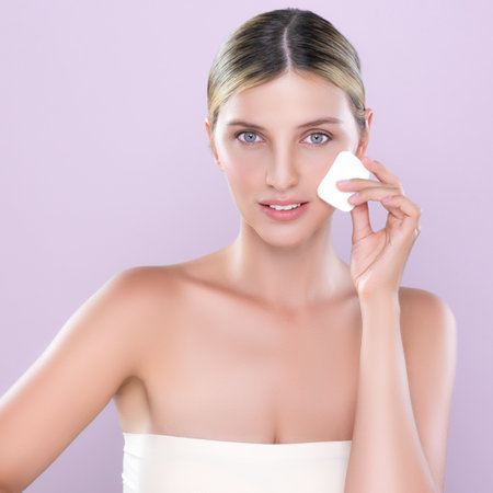 Alluring beautiful female model applying powder puff for facial makeup concept. Portrait of flawless perfect cosmetic skin woman put powder foundation on her face in pink isolated background.の写真素材