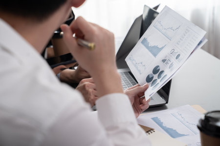 Focus closeup on BI dashboard on meeting desk with blur businesspeople in background analyzing data report with hands pointing on financial paper as concept of harmony in office workplace.の写真素材