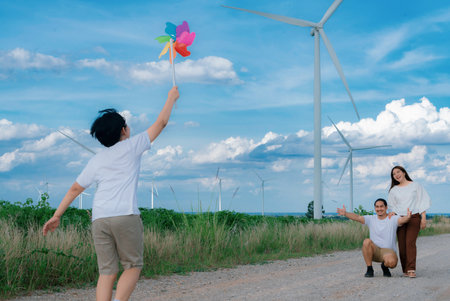 Progressive happy family enjoying their time at wind farm for green energy production concept. Wind turbine generators provide clean renewable energy for eco-friendly purposes.の写真素材
