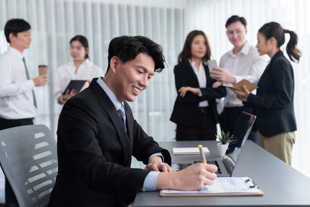 Portrait of focus young successful confident male manager, executive wearing business wear in harmony office arm crossed with blurred meeting background of colleagues, office worker.の写真素材
