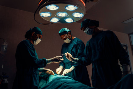 Surgical team performing surgery to patient in sterile operating room. In a surgery room lit by a lamp, a professional and confident surgical team provides medical care to an unconscious patient.の写真素材