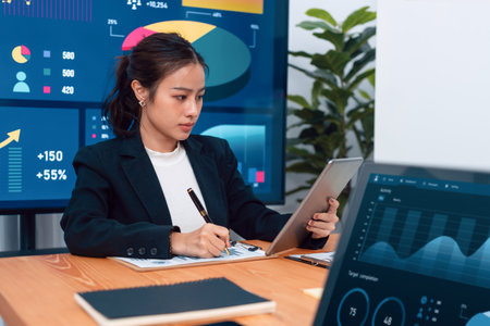 Focus portrait of female manger, businesswoman in the harmony meeting room with blurred of colleagues working together, analyzing financial paper report and dashboard data on screen in background.の写真素材