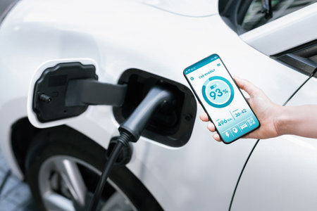 Battery status of electric vehicle displayed on smartphone application or software while vehicle is plugged into charging station for progressive future refueling. Battery status on phone screen.の写真素材