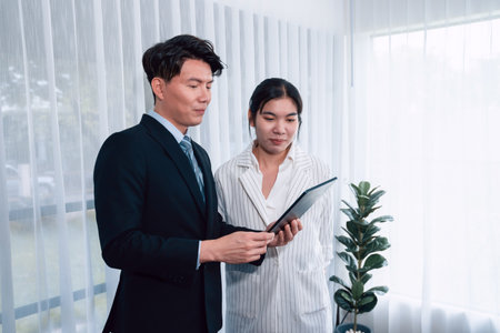 Manager advising guiding younger colleague with tablet in workplace. Couple businesspeople in formal wear working together on financial strategy as concept of teamwork and harmony in office.の写真素材