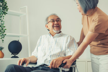 Senior wife giving support to her husband in his wheelchair with love, contented pensioner life. A senior couple is understanding and smiling at each other.の写真素材
