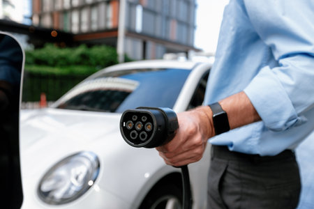 Closeup progressive man holding EV charger plug from public charging station for electric vehicle with background of residential building as concept eco-friendly sustainability energy car concept.の写真素材