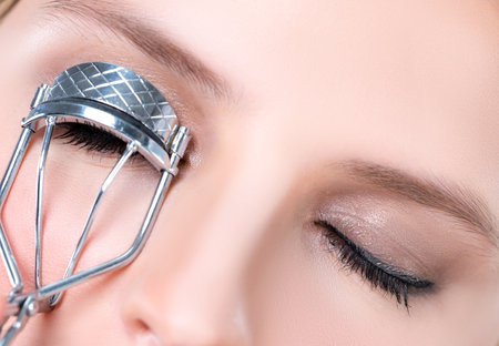Closeup alluring facial makeup, beautiful woman with perfect smooth cosmetic clean skin correct eyelash curler with metal mechanic beauty accessory in isolated background.の写真素材