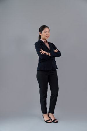 Full body length image of confident young businesswoman stands on isolated background, posing in formal black suit. Office lady or manager with smart and professional appearance. Enthusiasticの写真素材