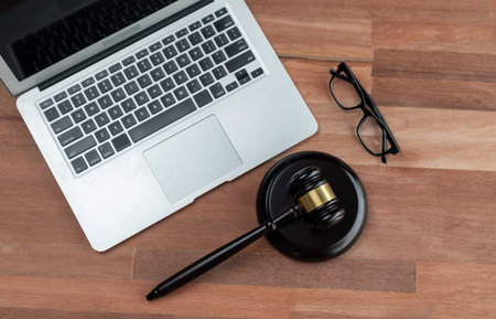 Closeup top view black wooden gavel hammer with laptop on wooden office desk or table background as justice and legal system by lawyer and judge, Symbolize authority and fairness in trial. equilityの写真素材