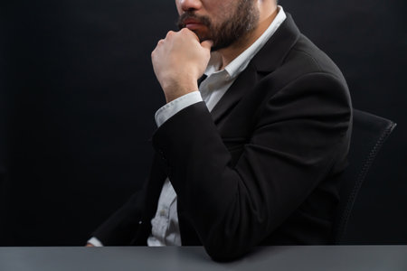 Businessman or lawyer wearing formal black suit sitting at table on isolated black background. Concept of a man with authority and seriousness gesture. equilityの写真素材