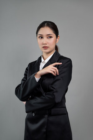 Confident young businesswoman stands on isolated background, posing in formal black suit. Office lady or manager with smart and professional appearance. Enthusiasticの写真素材