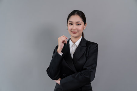 Confident young businesswoman stands on isolated background, posing in formal black suit. Office lady or manager with smart and professional appearance. Enthusiasticの写真素材