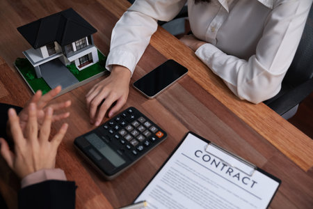 Reviewing house loan contract with agent. Analyzing financial documents and tax rates with calculator for ownership of property. Key signature for new home purchase and financing. Enthusiasticの写真素材
