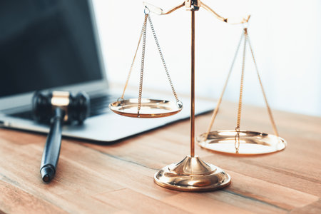 Symbolizing justice and legal authority, golden balanced scale and gavel on desk with laptop in law office background, reflecting concept of equality and fair judgment by lawyer and judge. equilityの写真素材
