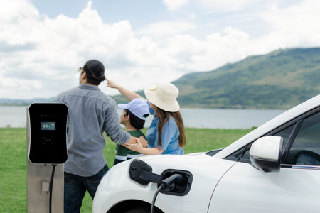 Concept of progressive happy family enjoying their time at green field and lake with electric vehicle. Electric vehicle driven by clean renewable from eco-friendly power sauce.の写真素材