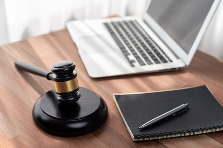 Closeup wooden gavel hammer with laptop and book and pen on desk on wooden office table background as justice legal system for lawyer and judge, Symbolize authority and fairness in trial. equilityの写真素材