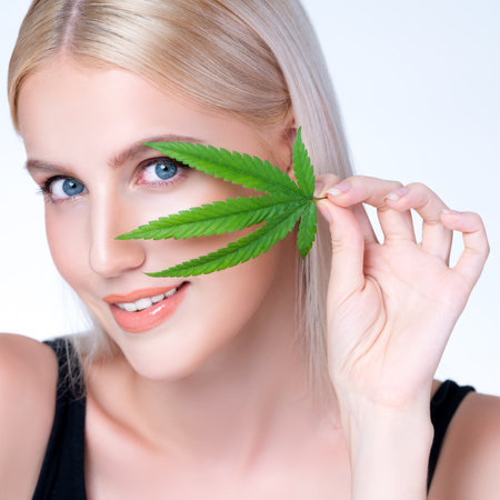 Closeup personable beautiful white blond hair with perfect smooth makeup skin hold cannabis green hemp in isolated background for natural CBD skincare treatment with perfect facial gesture expression.の写真素材