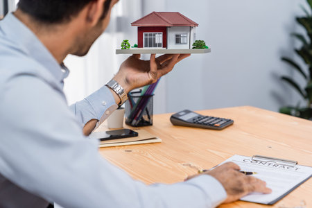 Client review loan contract and holding house sample model. Analyzing legal document, reading agreement on term, interest and property ownership before deciding. Real estate business. Ferventの写真素材