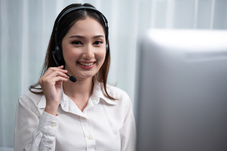 Asian call center with headset and microphone working on her workspace looking at camera. Female operator provide exceptional customer service. Supportive call center agent portrait. Enthusiasticの写真素材