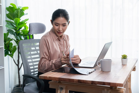 Young asian enthusiastic businesswoman at modern office desk using laptop to work and write notes. Diligent and attractive office lady working on computer notebook in her office work space.の写真素材