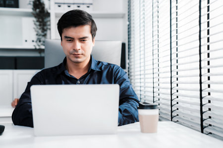 Competent male employee sits at his desk with a cup of coffee. Modern employee working with a drink, recreation during working hours, caffeine for office workers.の写真素材
