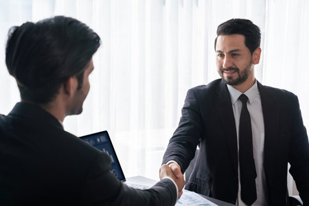Closeup professional businessman shaking hands over desk in modern office after successfully analyzing pile of dashboard data paper as teamwork and integrity handshake in workplace concept. ferventの写真素材