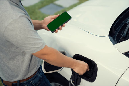 Mockup phone with green screen display energy status of electric vehicle connected to charging...