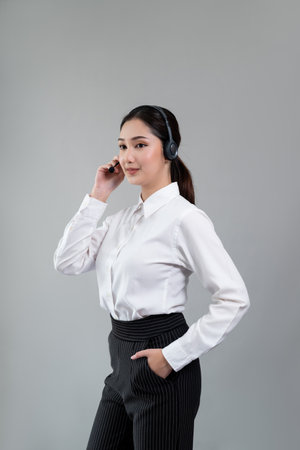 Attractive asian female call center operator with happy smile face advertises job opportunity on empty space, wearing a formal suit and headset on customizable isolated background. Enthusiasticの写真素材