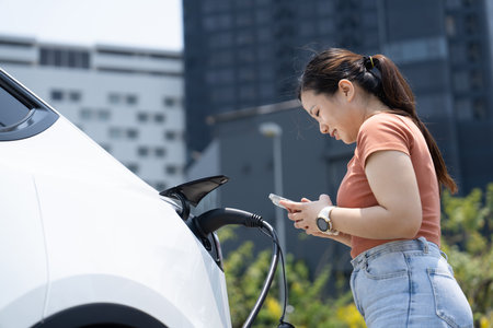 A young woman and her electric car at electric charging station in city center . EV urban lifestyle conceptの写真素材