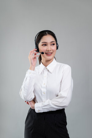 Attractive asian female call center operator with happy smile face advertises job opportunity on empty space, wearing a formal suit and headset on customizable isolated background. Enthusiasticの写真素材