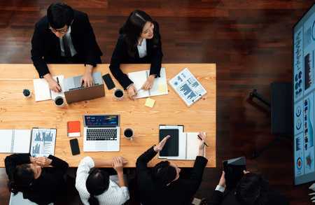 Top view manager or office worker give presentation in harmony conference room to business colleague, BI data dashboard on screen and pile of financial analyzed data reports on meeting table.の写真素材