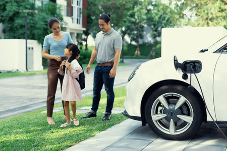 Progressive young happy family with electric vehicle and home backyard charging station. Green and clean energy from electric vehicles for healthy environment. Eco power from renewable source.の写真素材