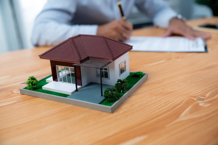 Focus house sample house model with blurred satisfied buyer sign house loan or purchase agreement with smile, finalizing the deal in the background with real estate agent or landlord. Ferventの写真素材