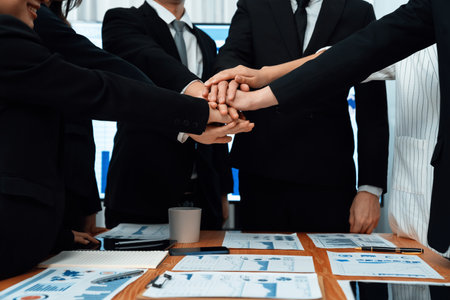Closeup business team of suit-clad businessmen and women join hand stack together and form circle. Colleague collaborate and work together to promote harmony and teamwork concept in office workplace.の写真素材