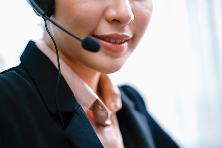 Asian call center with headset and microphone working on her workspace looking at camera. Female operator provide exceptional customer service. Supportive call center agent portrait. Enthusiasticの写真素材