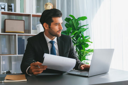 Modern professional businessman at modern office desk using laptop to work and write notes. Diligent...